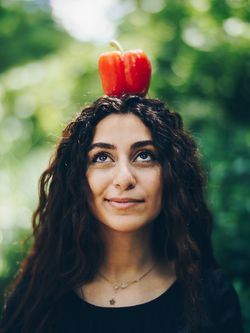 Frau mit dunklen Haaren und einer roten Paprika auf dem Kopf