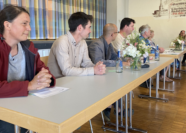 KI generiert: Eine Gruppe von Menschen sitzt an einem Tisch in einer Versammlung.
