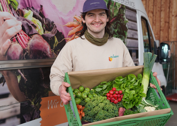 KI generiert: Ein Mann hält eine Kiste mit frischem Gemüse vor einem Lieferwagen.