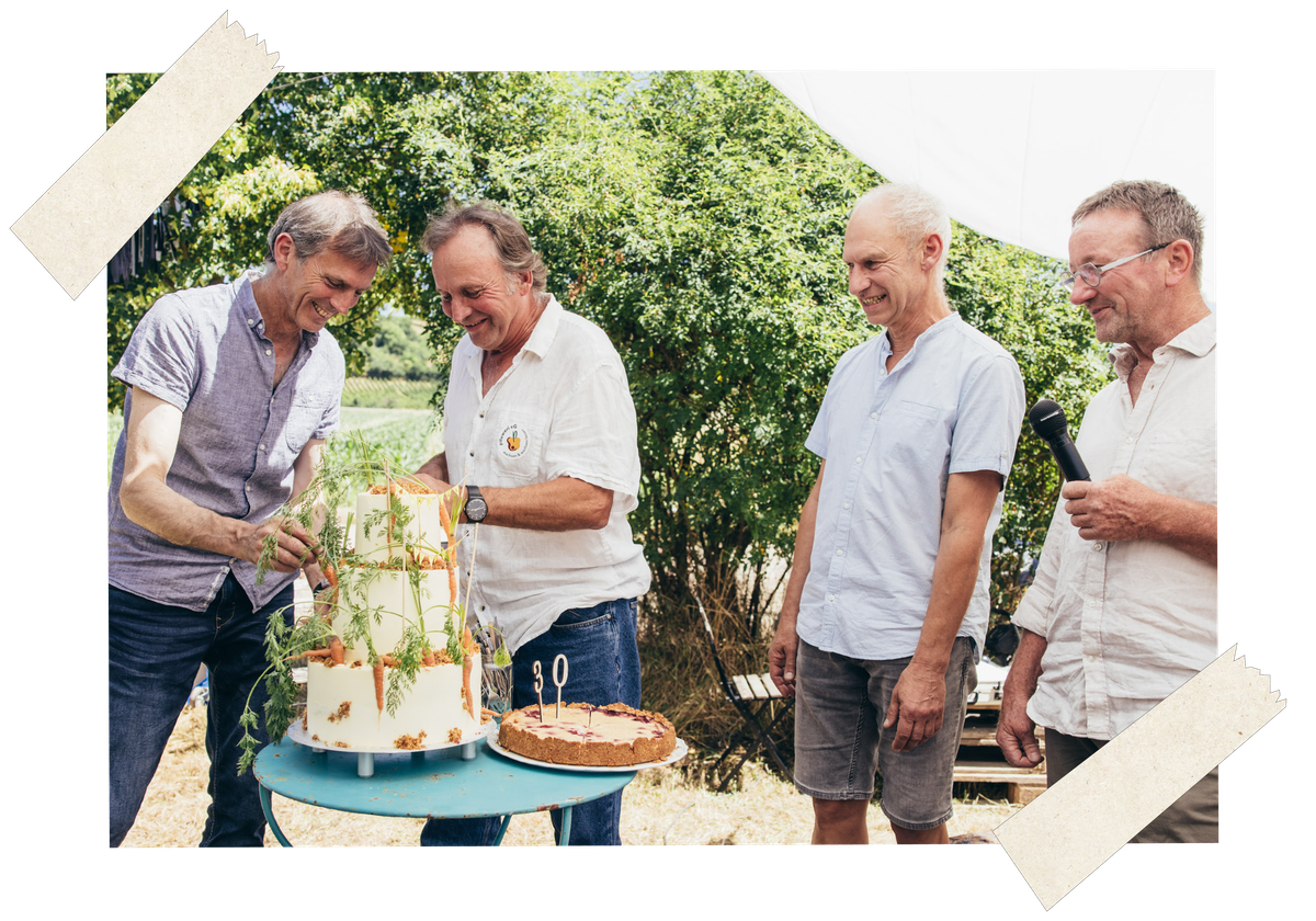 KI generiert: Vier Männer stehen um einen dekorierten Kuchen. Im Hintergrund ist Natur zu sehen.