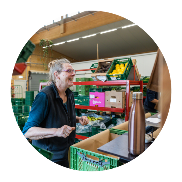 KI generiert: Eine Person in einem Lager mit Kisten voller Obst und Gemüse, lachend bei der Arbeit.