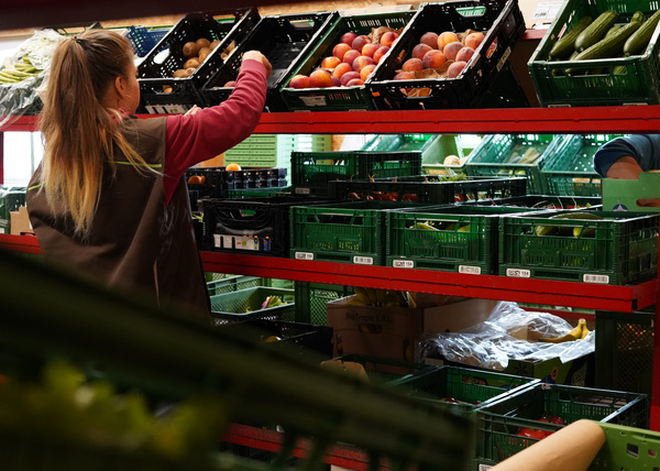 KI generiert: Eine Person sortiert Obst und Gemüse in einem Lager mit grünen Plastikkisten.