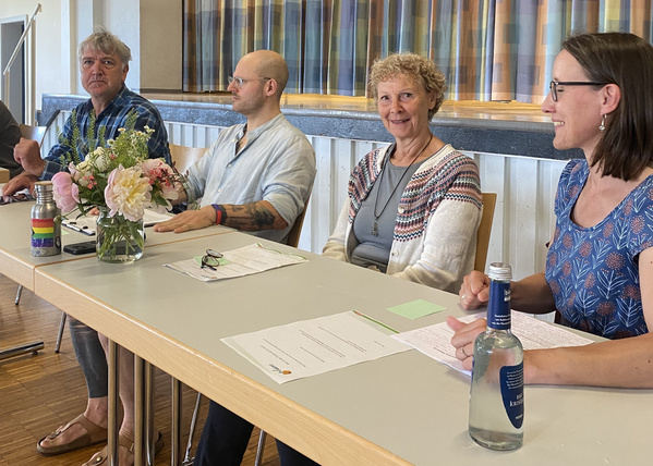 KI generiert: Eine Gruppe von Personen sitzt an einem Tisch mit Papier und Getränken. Ein Blumenstrauß steht auf dem Tisch.
