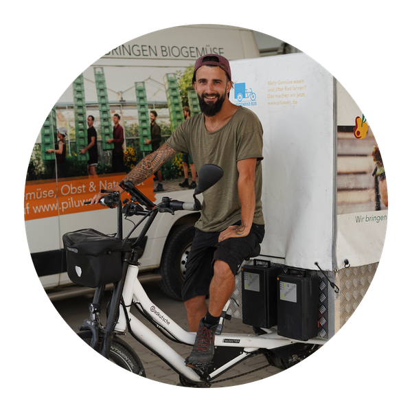 KI generiert: Eine Person auf einem Lastenfahrrad vor einem Transporter mit Werbung für Biogemüse. Text: "Wir bringen Biogemüse".