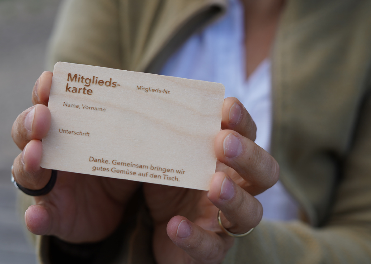 KI generiert: Hauptinhalt: Hände halten eine Mitglieds-Karte einer Ökokiste. Text: "Mitgliedskarte", "Danke. Gemeinsam bringen wir gutes Gemüse auf den Tisch."