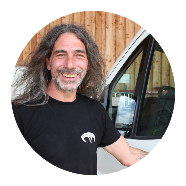 KI generiert: Ein Mann mit langen Haaren lächelt vor einem weißen Fahrzeug in die Kamera.