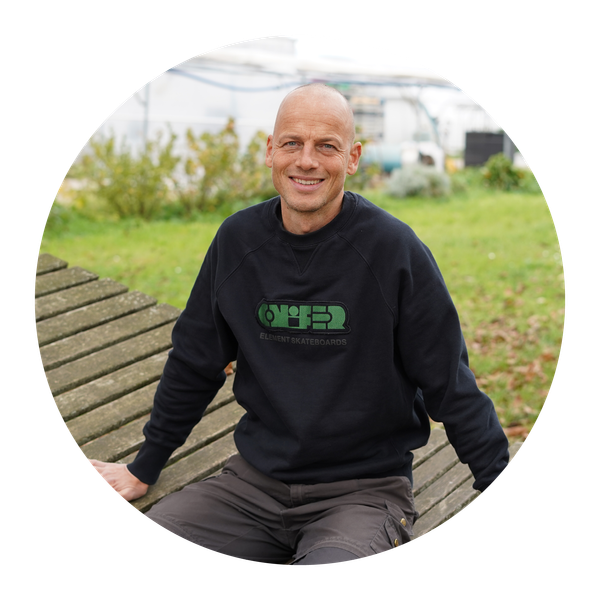 KI generiert: Ein Mann sitzt draußen auf einer Holzbank und lächelt. Er trägt ein Sweatshirt von Element Skateboards.