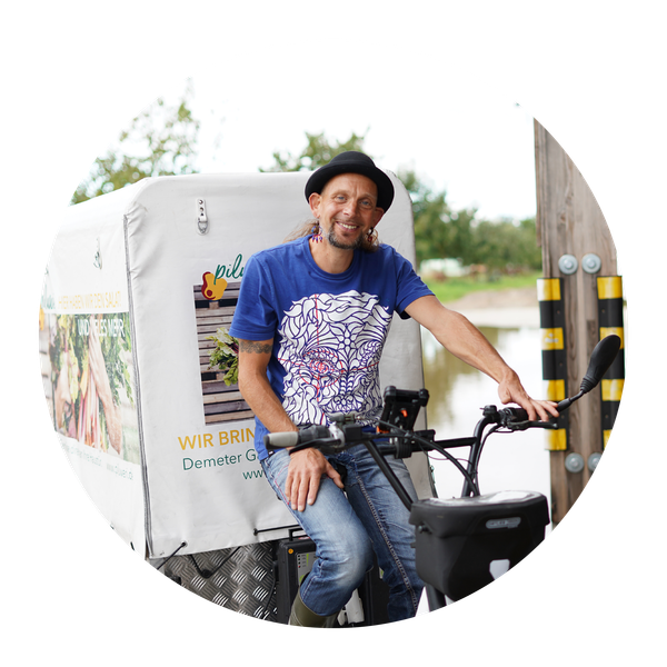 KI generiert: Ein Mann sitzt auf einem Lastenfahrrad. Text: „WIR BRINGEN... Demeter“.