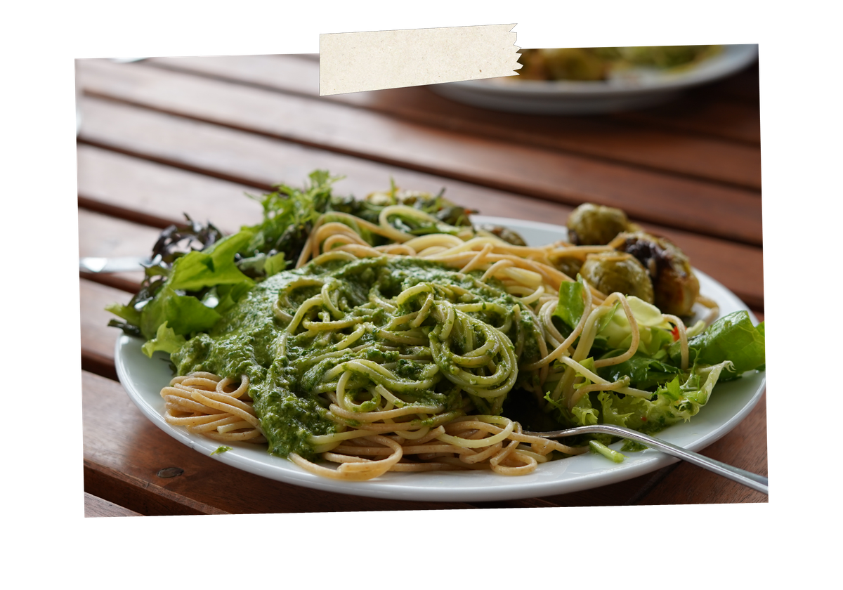KI generiert: Spaghetti mit grünem Pesto und frischem Salat auf einem Teller.