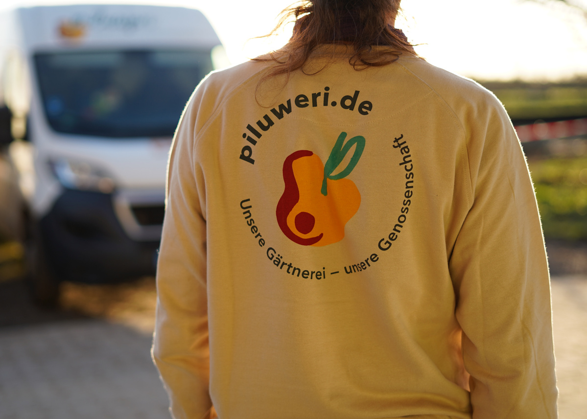 KI generiert: Eine Person zeigt den Rücken mit einem Shirt-Logo: "piluweri.de - Unsere Gärtnerei – unsere Genossenschaft".
