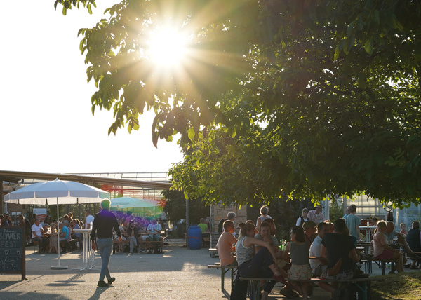 KI generiert: Menschen sitzen an Tischen im Freien bei Sonnenschein; ein Schild mit "SOMMER FEST" ist sichtbar.