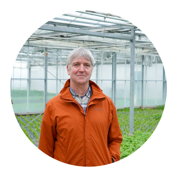 KI generiert: Ein Mann in einer orangen Jacke steht in einem Gewächshaus.