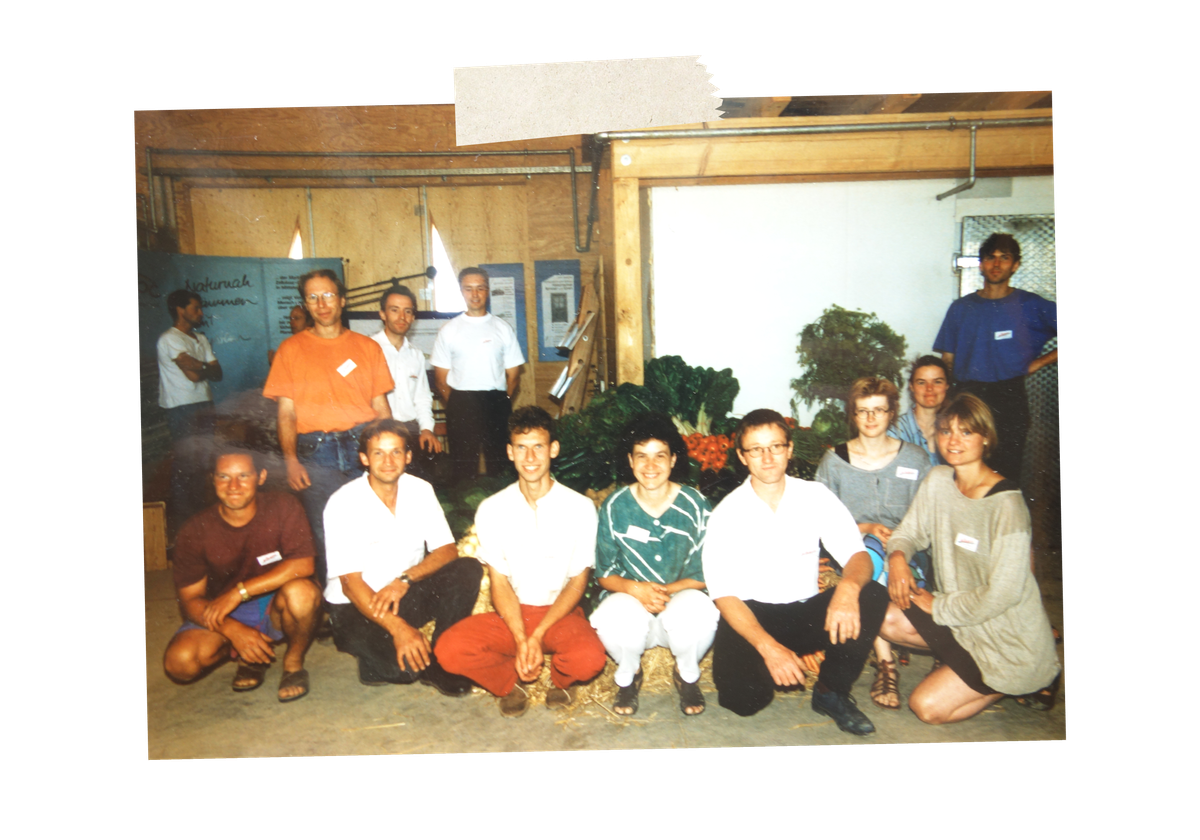 Das Gründungsteam von Piluweri Mitte der 90er Jahre posiert auf Strohballen und mit Gemüse im Hintergrund in der Halle.