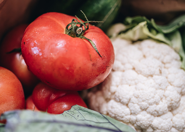 Eine Nahaufnahme von reifen, roten Tomaten, Blumenkohl und Kohlrabiblättern.