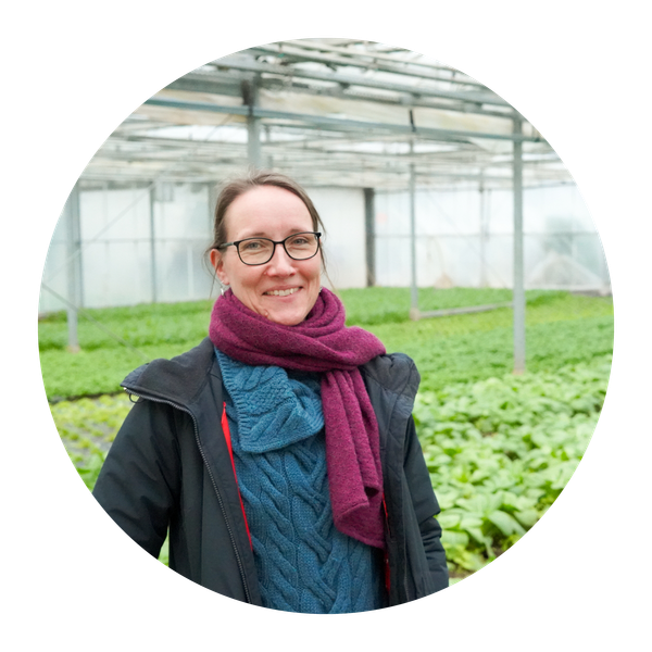 KI generiert: Eine Person steht lächelnd in einem Gewächshaus mit Pflanzen im Hintergrund.