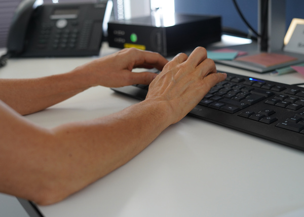 KI generiert: Hände tippen auf einer Tastatur im Büro; im Hintergrund ist ein Telefon zu sehen.