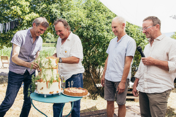 KI generiert: Vier Männer stehen um einen Tisch mit einer Torte im Freien.