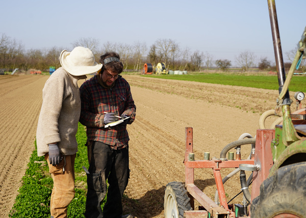 KI generiert: Zwei Personen prüfen Dokumente auf einem Acker neben einem Traktor.