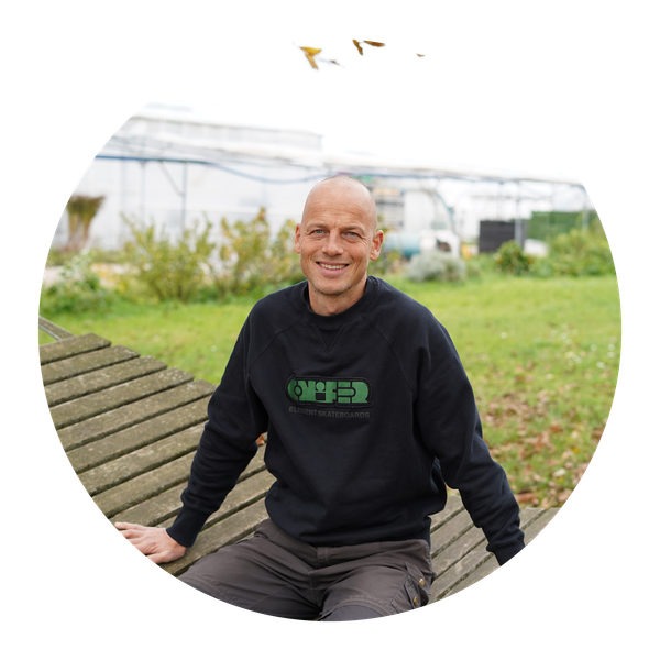 KI generiert: Ein lächelnder Mann sitzt im Freien auf einer Holzbank. Text: "ELEMENT SKATEBOARDS".