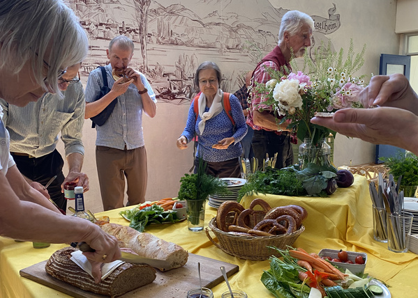 KI generiert: Menschen bedienen sich an einem Buffet mit Brot, Gemüse und Brezeln.