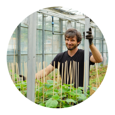 KI generiert: Ein Mann arbeitet in einem Gewächshaus und lächelt in die Kamera.