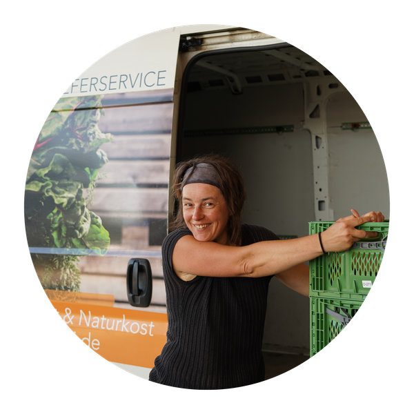 KI generiert: Eine Person lächelt und lädt grüne Kisten in einen Lieferwagen. Text: "Lieferservice & Naturkost".