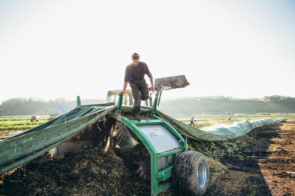 KI generiert: Ein Landwirt arbeitet mit einer Maschine auf einem Feld bei Sonnenaufgang.