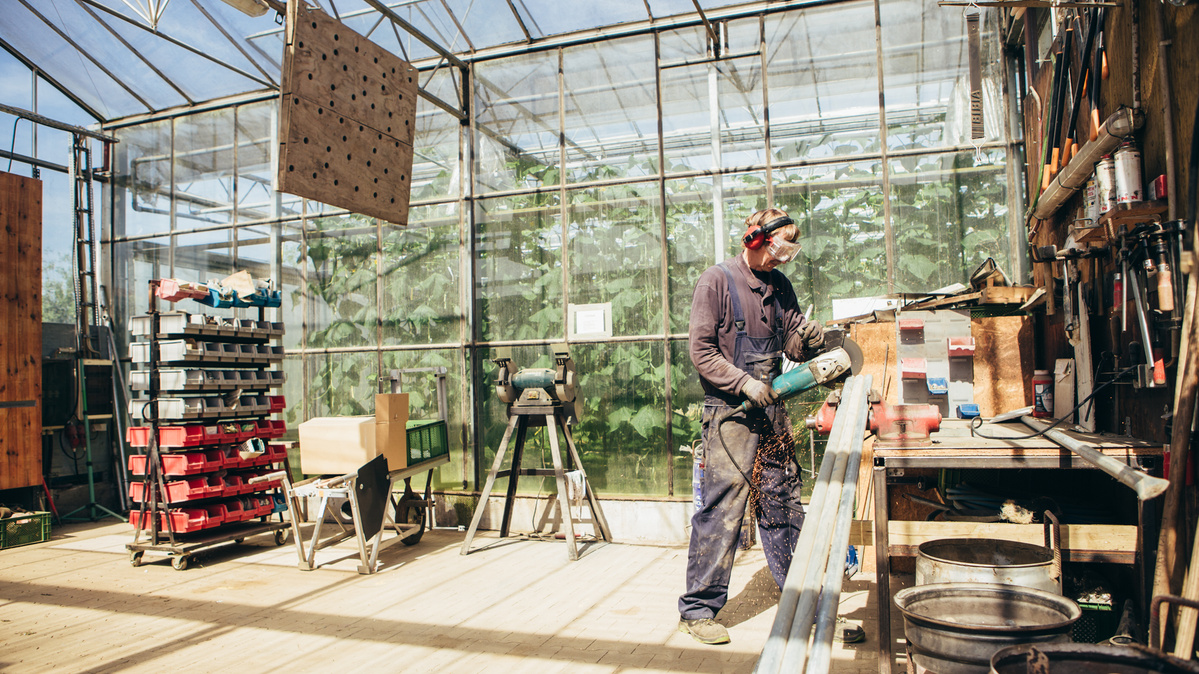 KI generiert: Ein Mann arbeitet mit Werkzeug in einer Werkstatt in einem Gewächshaus.