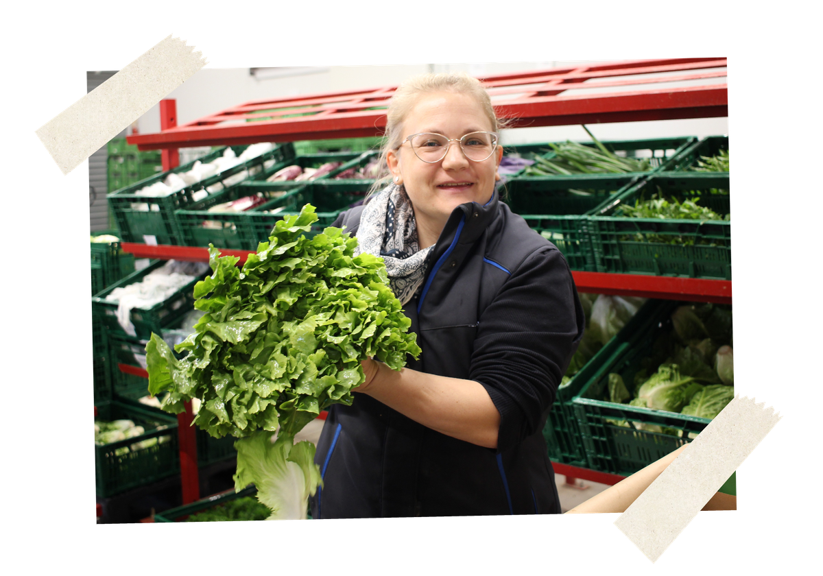 KI generiert: Eine Person hält einen frischen Salat vor Kisten mit Gemüse.