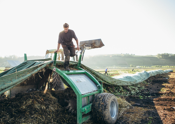KI generiert: Ein Mann arbeitet an einem Kompostiergerät auf einem Feld.
