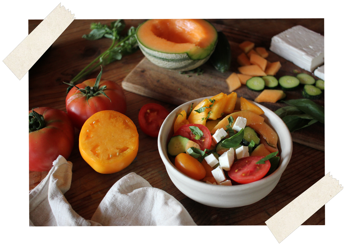 KI generiert: Frischer Salat mit Tomaten, Melonen, Gurken, Basilikum und Käse in einer Schüssel auf einem rustikalen Holztisch.