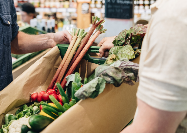 Ein Piluweri-Mitarbeiter hält eine  gepackte Abokiste in der Hand. In der Kiste sind Radieschen, Blumenkohl, Paprika, Gurken, Salat und Rhabarber.