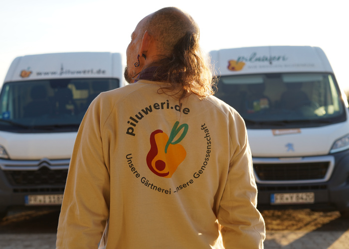 Ein Mann steht vor zwei Piluweri-Transportern. Er hat ein Sweatshirt von Piluweri an.